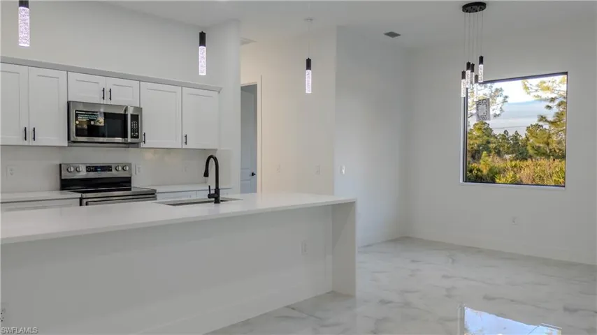 Kitchen featuring light stone countertops, white cabinets, appliances with stainless steel finishes, decorative light fixtures, and light marble finish floors