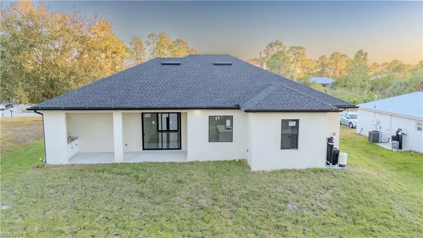 Back of house at dusk with stucco siding, a yard, a patio area, and roof with shingles