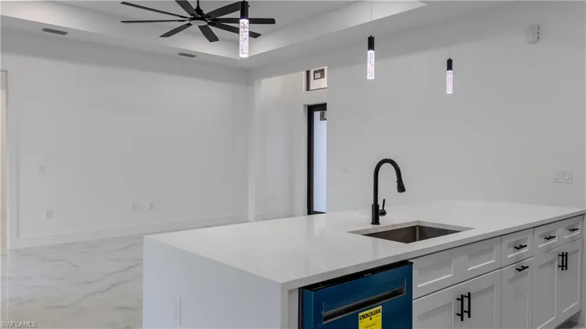 Kitchen with pendant lighting, a raised ceiling, white cabinetry, light stone counters, and dishwasher