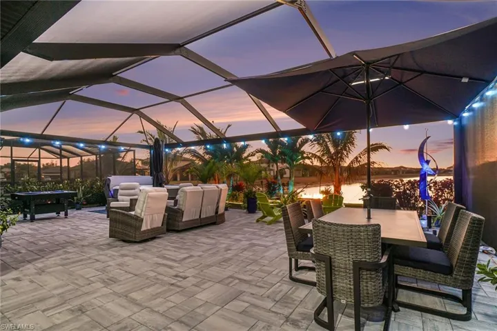 Patio terrace at dusk featuring an outdoor living / dining area, a sunroom, a patio area, glass enclosure, and a water view