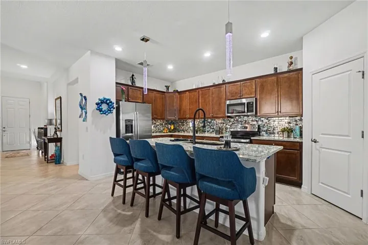 Kitchen with a kitchen breakfast bar, a kitchen island with sink, hanging light fixtures, light stone countertops, and stainless steel appliances