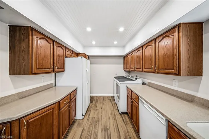 Kitchen featuring white appliances, brown cabinets, light wood finished floors, recessed lighting, and washing machine and clothes dryer