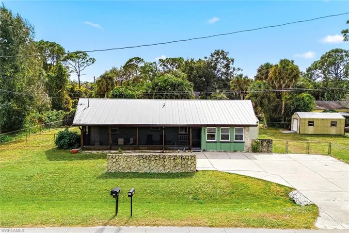 View of front of home with a metal roof, concrete driveway, a sunroom, and view of scattered trees