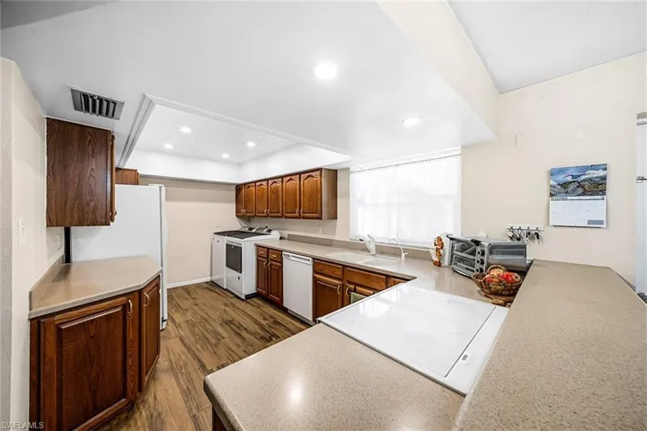 Kitchen with light countertops, white appliances, dark wood finished floors, recessed lighting, and brown cabinets