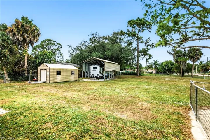 Fenced backyard with a carport, an outdoor structure, a patio area, and view of wooded area