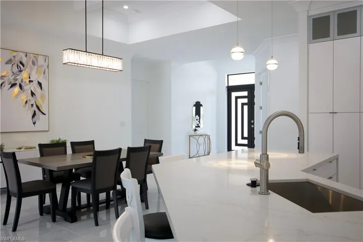 Tiled dining space with a notable chandelier, sink, a raised ceiling, and crown molding