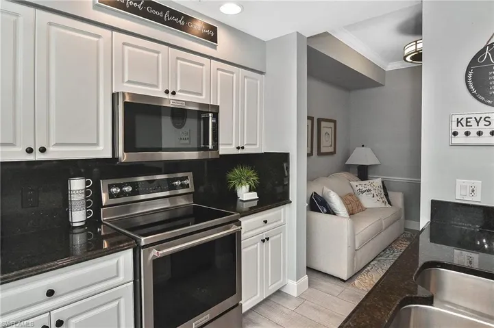 Kitchen with appliances with stainless steel finishes, crown molding, white cabinetry, dark stone countertops, and light wood-type flooring