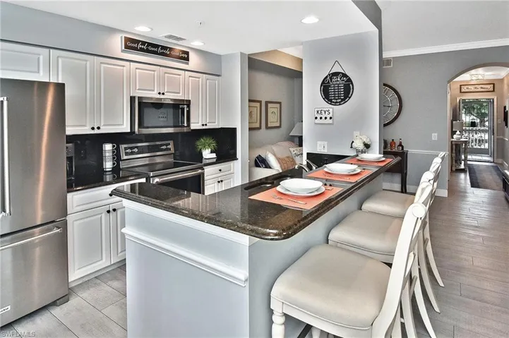 Kitchen with appliances with stainless steel finishes, crown molding, light wood finished floors, a breakfast bar, and arched walkways