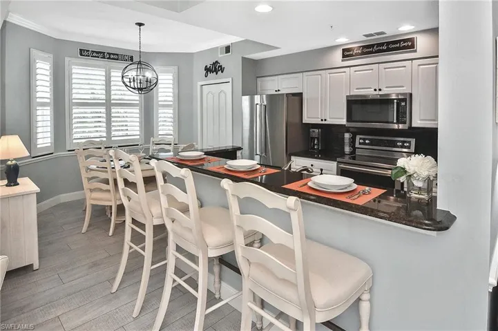 Kitchen with stainless steel appliances, light wood-type flooring, dark countertops, white cabinets, and a breakfast bar