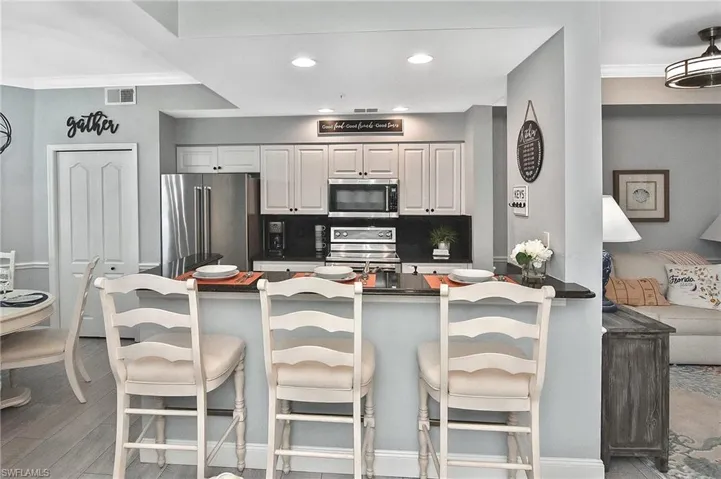 Kitchen with crown molding, appliances with stainless steel finishes, a breakfast bar area, recessed lighting, and dark countertops