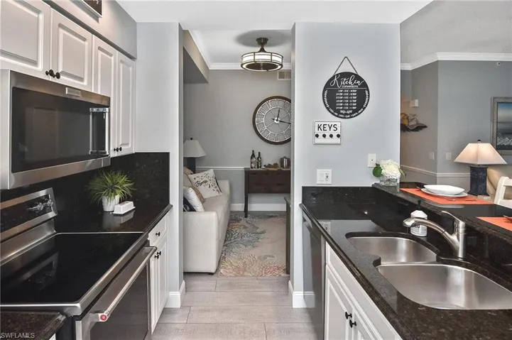 Kitchen with appliances with stainless steel finishes, ornamental molding, white cabinets, light wood finished floors, and dark stone countertops