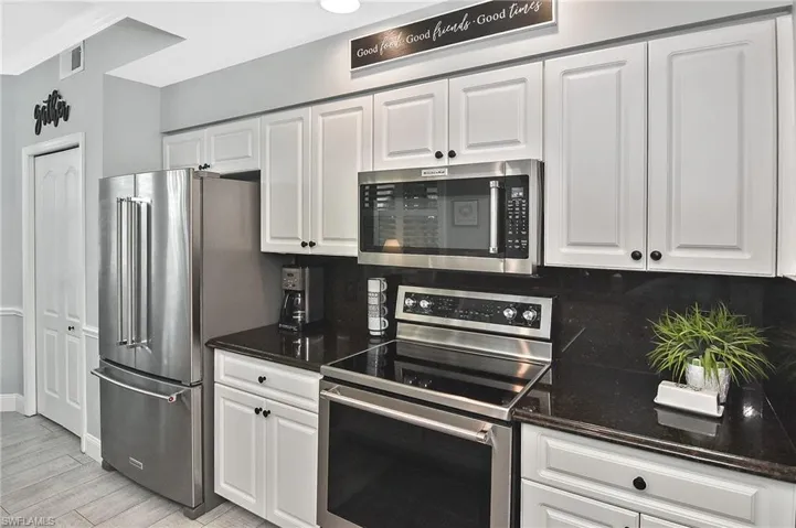 Kitchen with stainless steel appliances, white cabinetry, crown molding, dark stone counters, and light wood finished floors