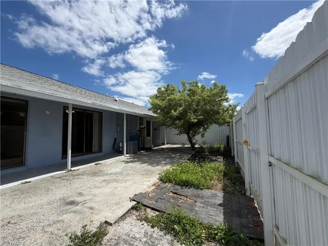 The property features a concrete patio area, a mature tree, and a light-colored fence enclosing the yard
