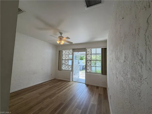 This room features wood-look flooring, a ceiling fan with integrated lighting, and windows with horizontal blinds and decorative glass blocks