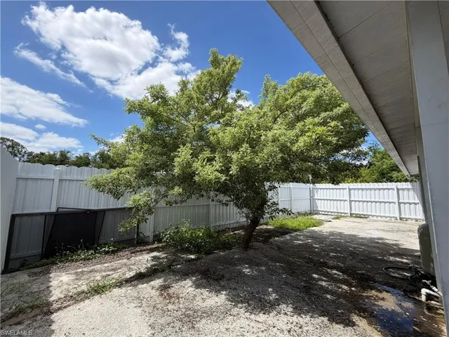 The property features an extensive backyard area with a mature tree, a white privacy fence, and a clear blue sky overhead