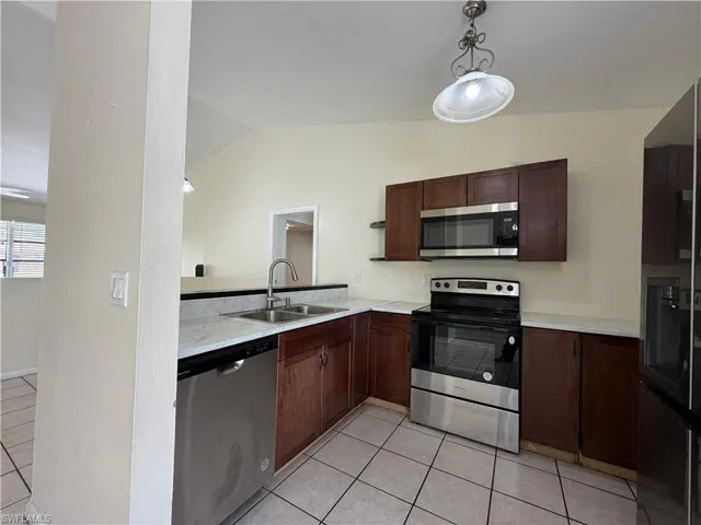 The kitchen features dark wood cabinetry, stainless steel appliances, a double basin sink, and tile flooring