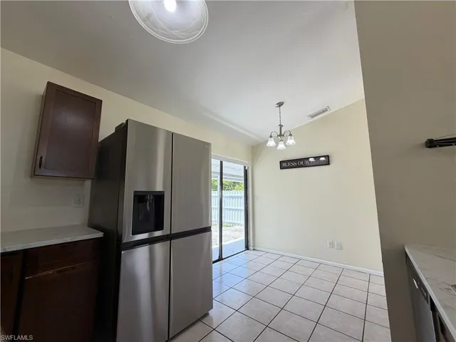 The kitchen features tiled flooring, a stainless steel refrigerator, and dark wood cabinetry with light-colored countertops