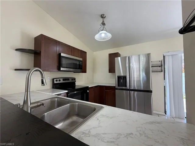 The kitchen features a double basin stainless steel sink with a gooseneck faucet, light-colored countertops, and dark wood cabinetry