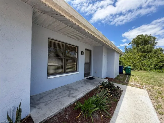 The property features a stucco exterior, a covered entryway, and a concrete pathway leading to the front door