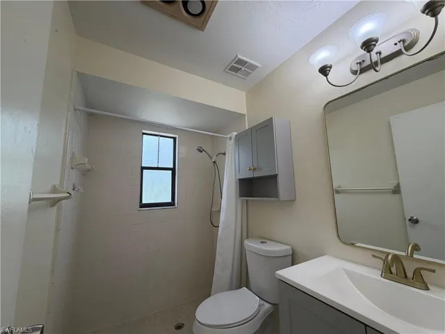 Bathroom featuring a shower with a window, a single vanity with a white countertop and gold-toned faucet, and a wall-mounted medicine cabinet