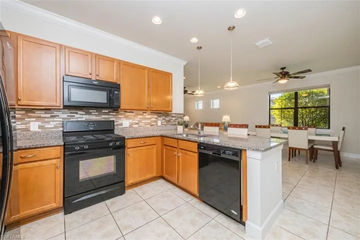 Kitchen with black appliances, light stone counters, a peninsula, ornamental molding, and a ceiling fan