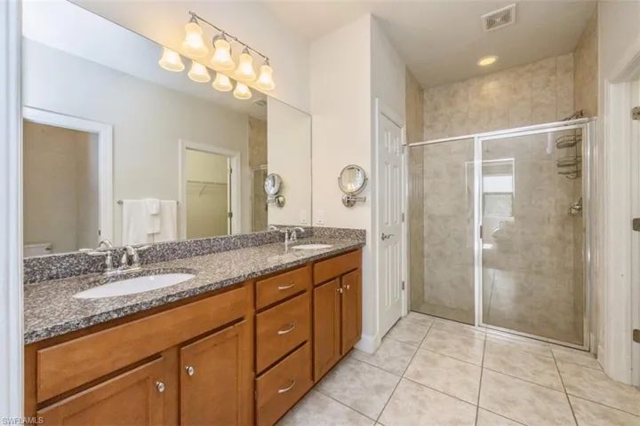 Bathroom with double vanity, a stall shower, light tile patterned flooring, and a walk in closet
