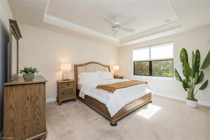 Carpeted bedroom featuring a raised ceiling and ceiling fan