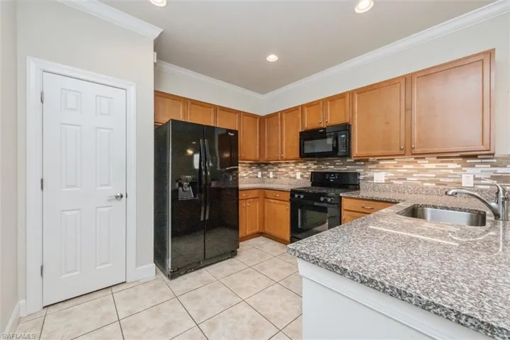 Kitchen with black appliances, light stone counters, crown molding, decorative backsplash, and light tile patterned floors