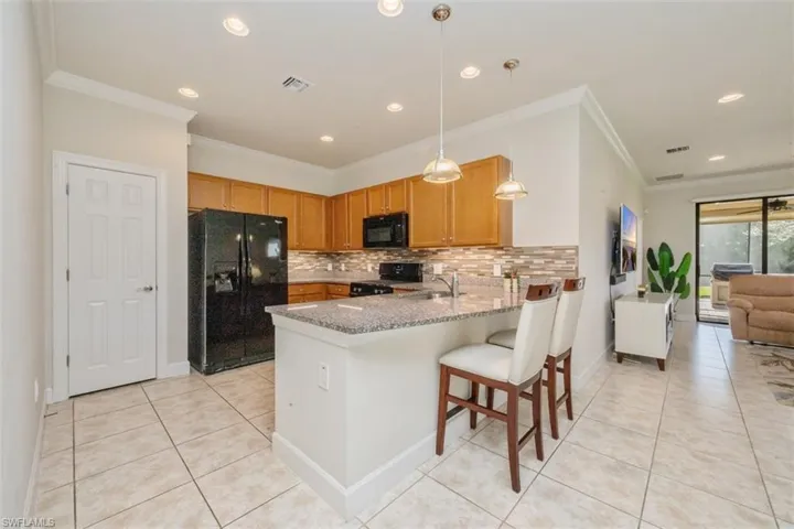 Kitchen with black appliances, pendant lighting, crown molding, a breakfast bar, and decorative backsplash