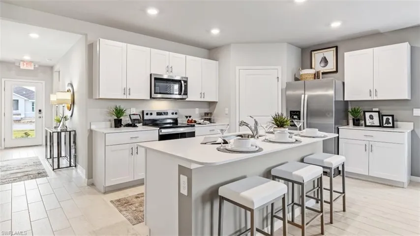 Model home. Kitchen with stainless steel appliances, white cabinets, a breakfast bar area, recessed lighting, and an island with sink