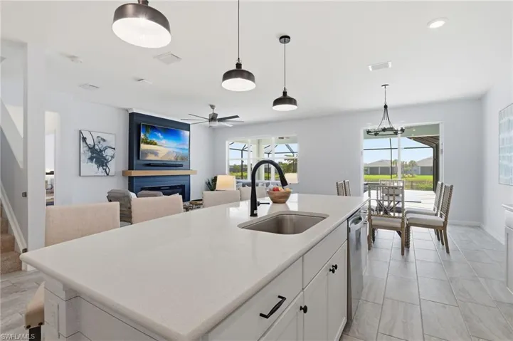 Kitchen featuring white cabinets, a fireplace, hanging light fixtures, a center island with sink, and a ceiling fan