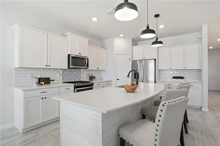 Kitchen with backsplash, white cabinets, an island with sink, and recessed lighting