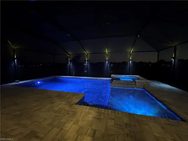 Pool at night featuring a pool with connected hot tub