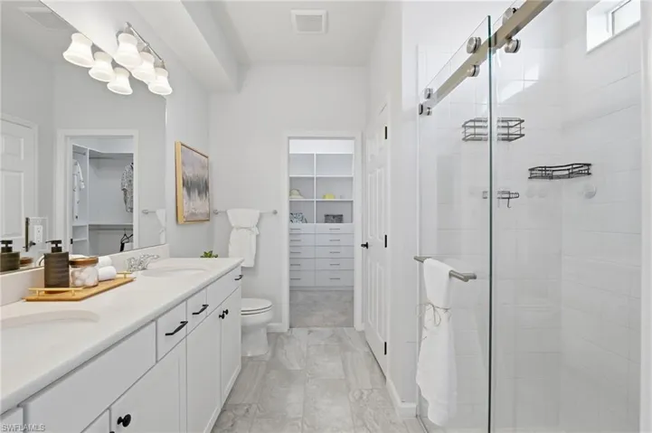 Bathroom with a walk in closet, double vanity, and a stall shower