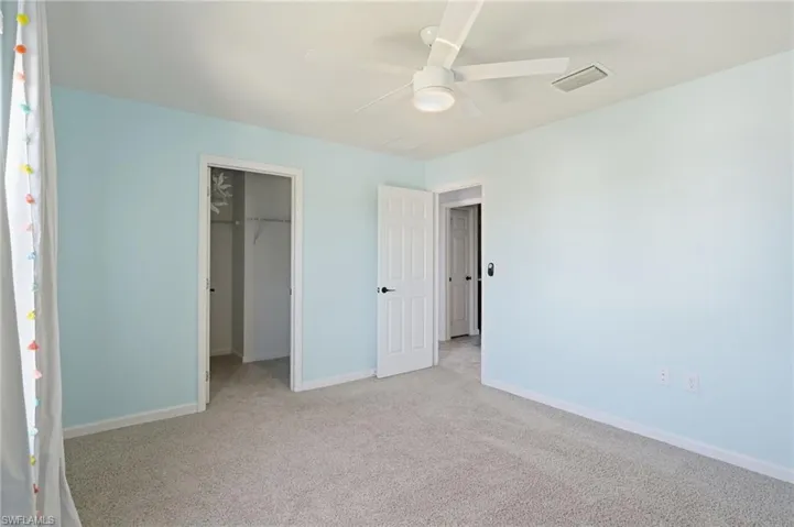 bedroom with carpet flooring, a walk in closet, and a ceiling fan Bedroom with walk in closet