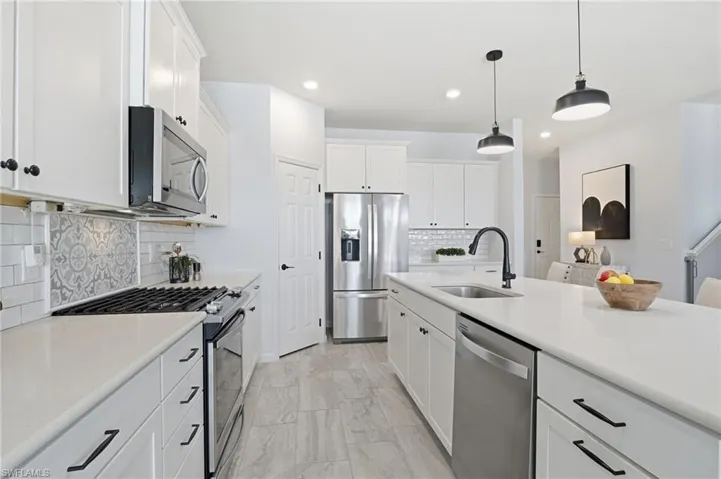 Kitchen featuring appliances with stainless steel finishes, white cabinets, hanging light fixtures, tasteful backsplash, and light stone counters