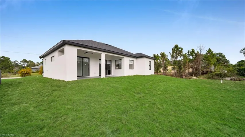 Back of property featuring ceiling fan, a patio area, a lawn, and stucco siding