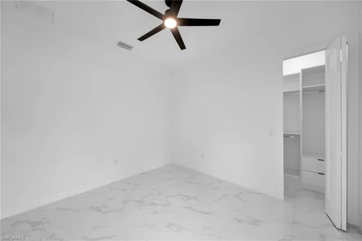 Unfurnished bedroom with light marble finish floors, a walk in closet, and a ceiling fan