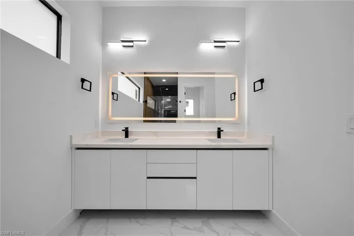 Full bath featuring double vanity, light marble finish floors, and a walk in shower