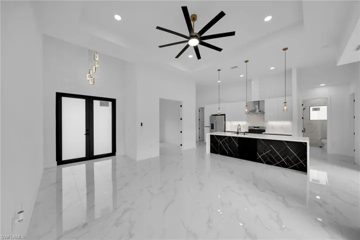 Kitchen featuring decorative light fixtures, a spacious island, open floor plan, light marble finish floors, and a high ceiling