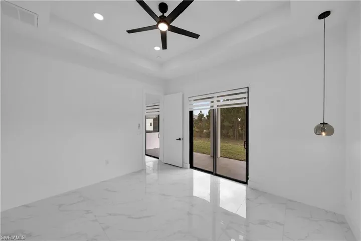 Empty room with a tray ceiling, light marble finish flooring, a ceiling fan, and recessed lighting