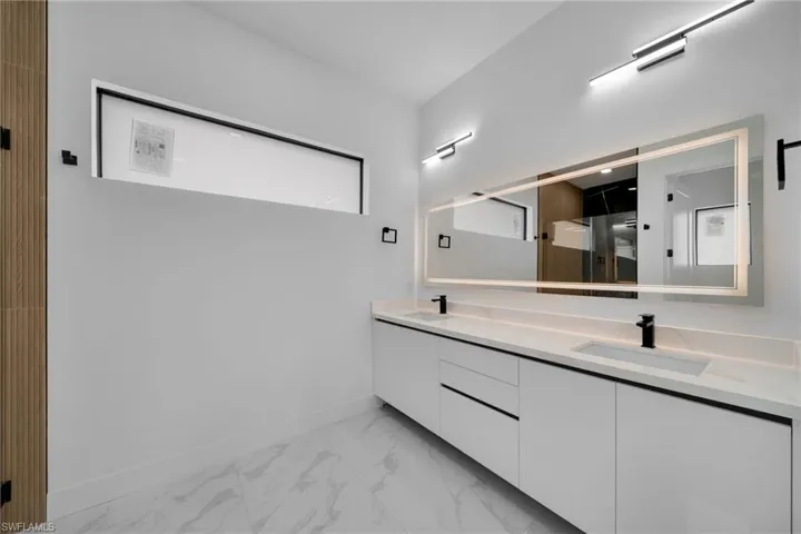 Bathroom with double vanity, light marble finish flooring, and a shower stall