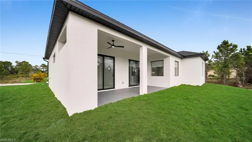 Rear view of house featuring a lawn, stucco siding, and a patio area
