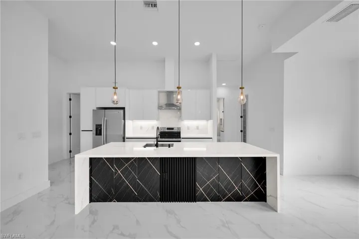 Kitchen with appliances with stainless steel finishes, light stone counters, an island with sink, hanging light fixtures, and recessed lighting