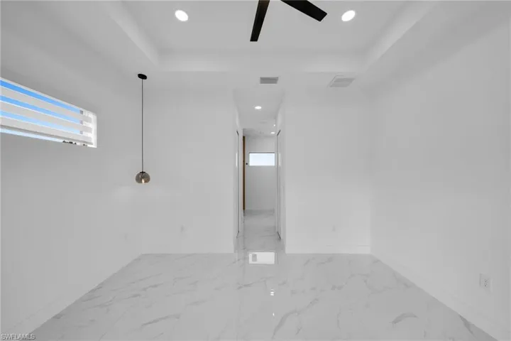 Spare room with plenty of natural light, light marble finish flooring, recessed lighting, a ceiling fan, and a raised ceiling
