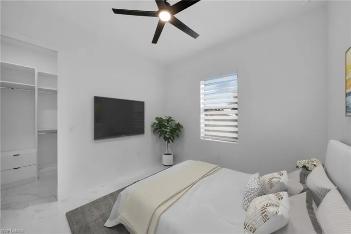 Bedroom featuring a walk in closet, light marble finish floors, and a ceiling fan