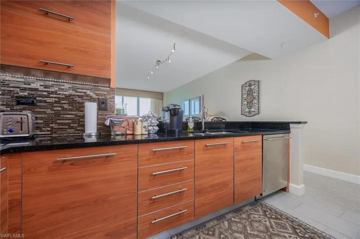 Kitchen featuring wood finish cabinets, dark stone counters, stainless steel dishwasher, tasteful backsplash, and modern cabinets