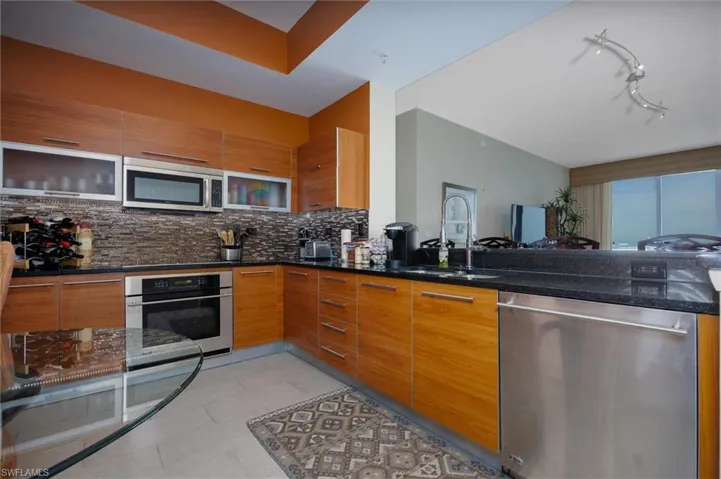 Kitchen featuring stainless steel appliances, dark stone counters, wood finish cabinets, modern cabinets, and a peninsula