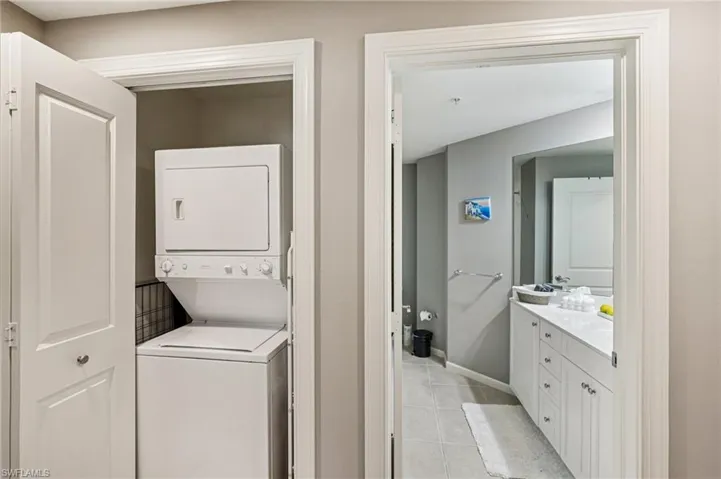 Washroom with stacked washing machine and dryer and light tile patterned flooring