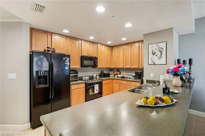 Kitchen featuring black appliances, light tile patterned floors, recessed lighting, a peninsula, and brown cabinetry